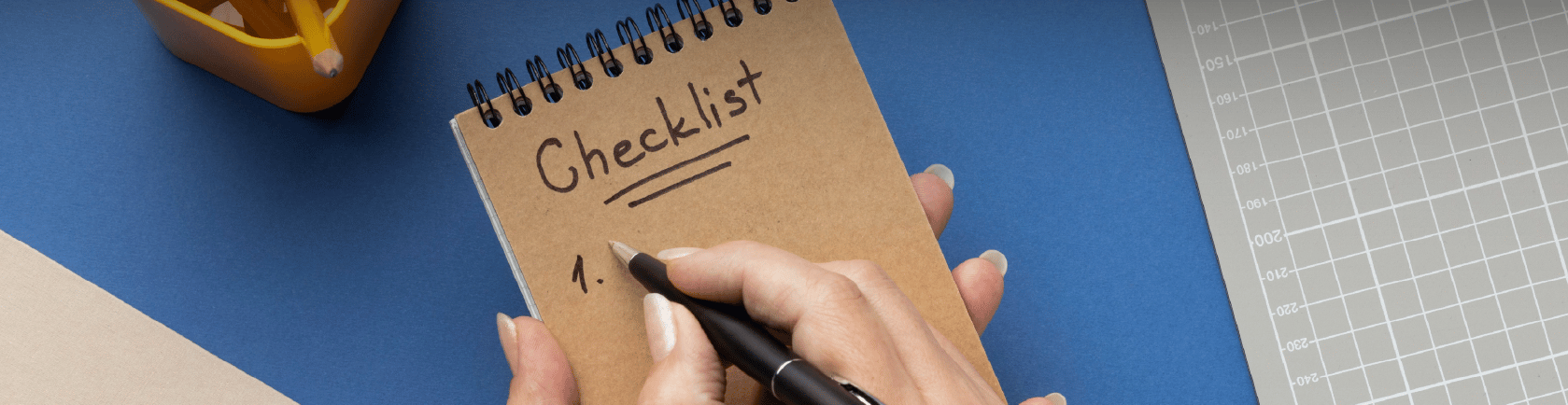 Vista superior de manos escribiendo en libreta con título Checklist sobre mesa azul